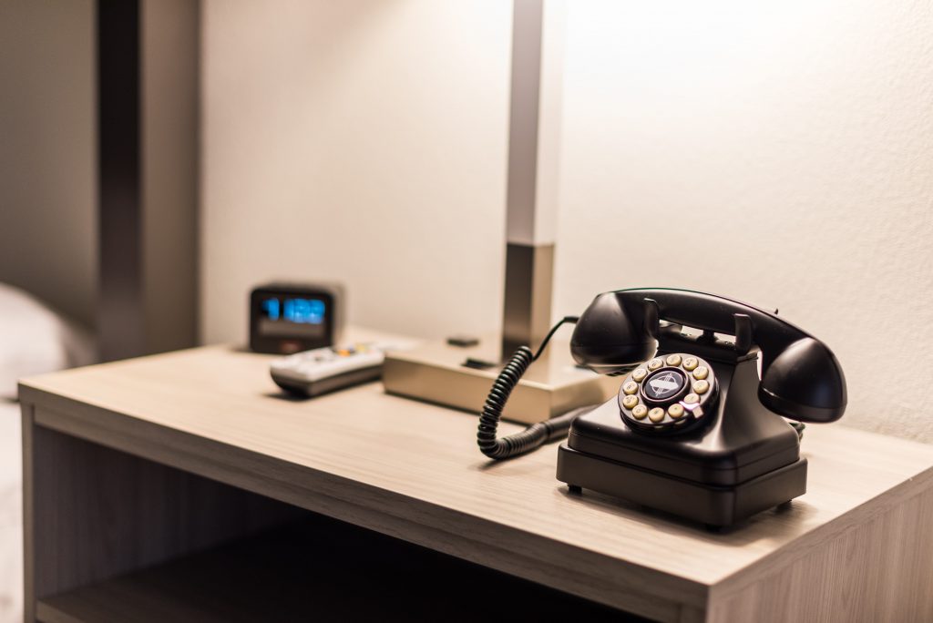 In-room amenities at Expedition Lodge Moab, including a telephone, bedside lamp, TV remote, and clock, providing convenience and comfort near Arches National Park.