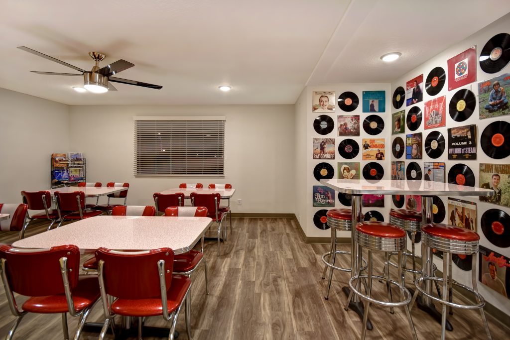 Lobby sitting area at Expedition Lodge Moab with retro tables, chairs, bar stools, and records on the wall, creating a vintage and cozy atmosphere.