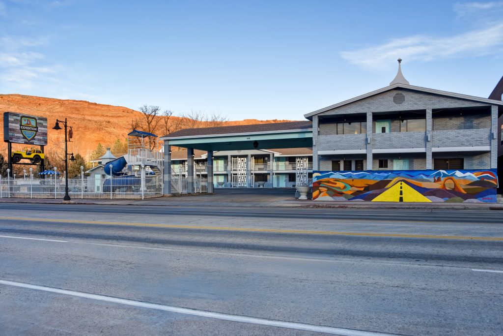 Exterior of Expedition Lodge Moab with drive, porte-cochère, and colorful mural, offering a welcoming entrance near Arches National Park.