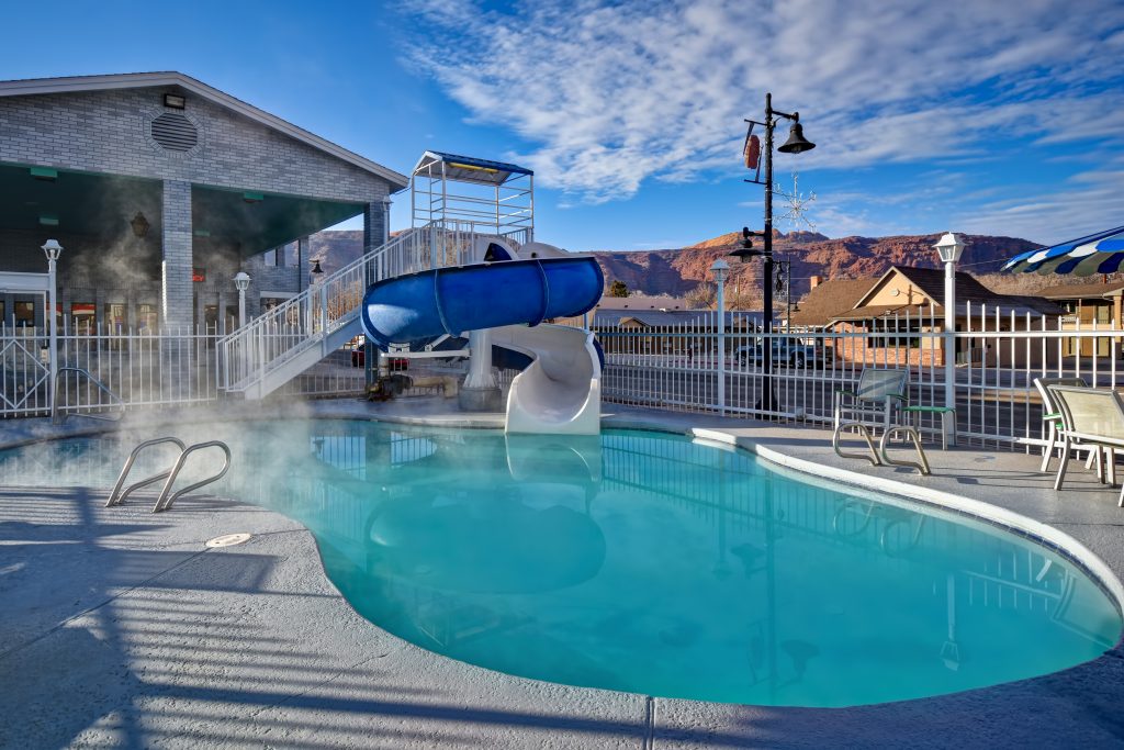 Outdoor pool at Expedition Lodge Moab with steam rising and retro-style hotel exterior in the background, near Arches National Park.